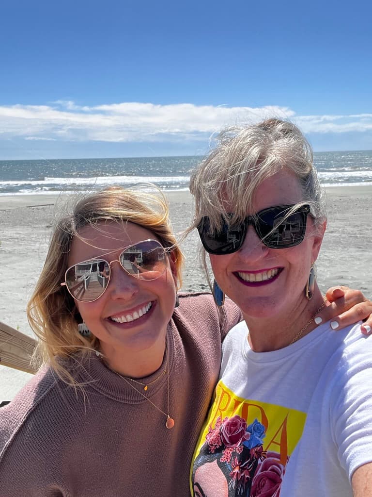 Cathy and a Sacred Interruption participant smiling on a sunny beach.